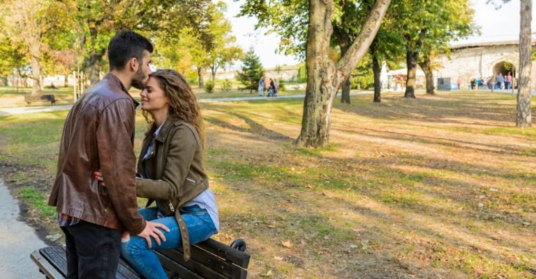 A loving couple enjoys a tender moment on a park bench surrounded by autumn trees.